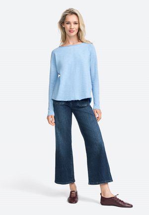 Maglietta azzurro chiaro a maniche lunghe con scollo a barca, abbinata a jeans a gamba larga blu scuro e scarpe stringate bordeaux. Tessuto texturizzato.