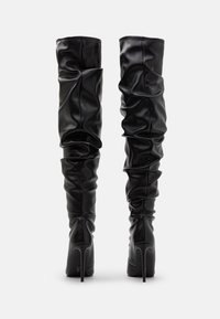 Schwarze Lederstiefel über dem Knie mit geraffter Textur, hohen Stiletto-Absätzen und abgerundeten Spitzen. Nahtdetails betonen das Design.