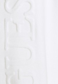 Un tessuto bianco presenta un testo in rilievo, enfatizzando la texture e il motivo. La superficie appare liscia con una leggera lucentezza, aumentando l'interesse visivo.