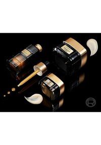 Trois contenants cosmétiques : une bouteille compte-gouttes brune, un pot noir avec des accents dorés, et un petit pot de crème, accompagnés d'échantillons de crème.