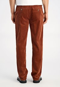 Brune bukser i kordfløjl med lodrette ribber, lige snit og to baglommer med metalnitter. Båret med sorte sko.