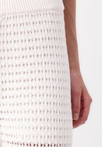 Weißes gestricktes Kleid mit strukturiertem Muster, ausgestattet mit einem gerippten Oberteil und einem offenen Design. Der Stoff ist leicht und luftig.