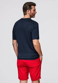 Mörkblå kortärmad tröja för män med rund hals, ihop med röda shorts. Tröjan har en strukturerad stickning och en figurnära design.