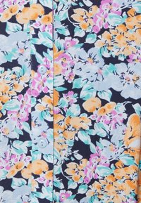 Camisa de botão floral com fundo azul marinho e flores em rosa, laranja e azul claro. Tecido de algodão, textura suave e dois botões visíveis.