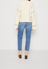 Cream ribbed sweater with dolman sleeves, paired with light blue straight-leg jeans and beige heeled ankle boots.