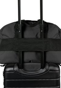Ein schwarzer Rollkoffer mit einem Griff, auf dem ein schwarzer Rucksack mit Riemen gesichert ist, zeigt eine kompakte Reisearrangement.