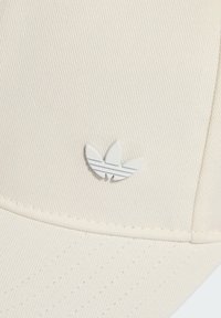 Béžová baseballová čepice s texturovanou látkou, s bílým logem se třemi listy a jemnými šedými pruhy. Čistý design a zakřivený kšilt.