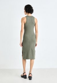 Olive green ribbed knit midi dress with a fitted silhouette, side slits, and sleeveless design. Worn with black platform sandals.