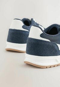 Marineblauwe en witte sneakers met een textured suède hak, een glad bovenwerk van synthetisch materiaal en een lichtbruine rubberen zool. Voorzien van een gewatteerde kraag en tong.