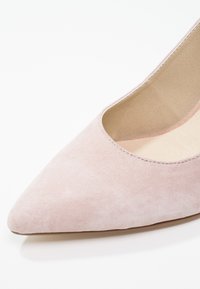 Escarpin en suède rose à bout pointu avec un design à décolleté, texture lisse et intérieur nude. Style minimaliste sans embellissements visibles.