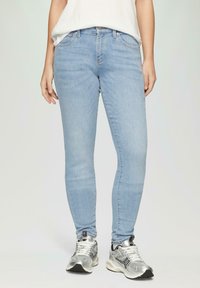 Jeans skinny bleu clair en denim, dotés de cinq poches, d'une taille mi-haute et d'un léger délavage, associés à des chaussures de sport argentées.