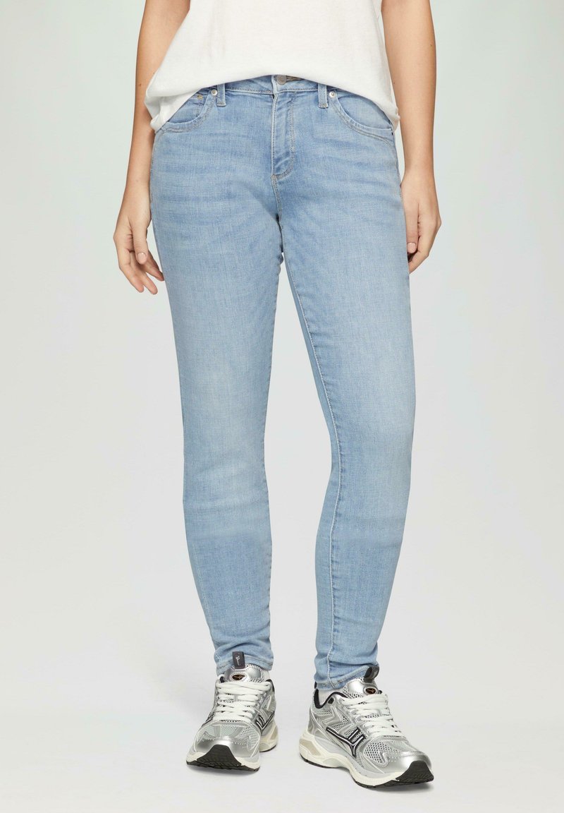 Jeans skinny bleu clair en denim, dotés de cinq poches, d'une taille mi-haute et d'un léger délavage, associés à des chaussures de sport argentées.