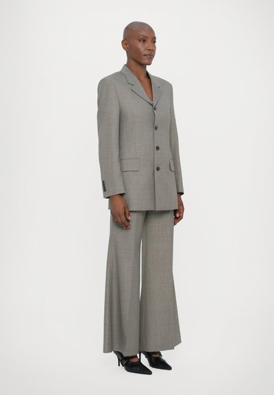Grijze geruite blazer met twee voorzakken, gecombineerd met wijde broekspijpen. Beide items hebben een op maat gemaakt ontwerp en knoopsluiting.