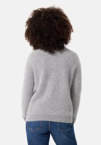 Maglione grigio realizzato in materiale morbido e peloso; presenta un collo tondo e una vestibilità comoda. Indossato con jeans blu, che mostrano un look casual.