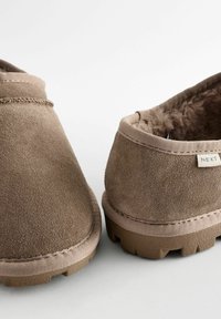 Chaussures à enfiler en suède marron avec un intérieur doux et moelleux, un contour en cuir de couleur tan contrastante et des semelles en caoutchouc texturé avec une adhérence à motif.