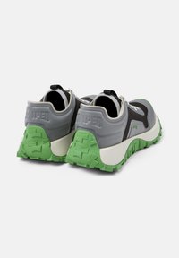 Graue und schwarze Sneakers mit einer strukturierten grünen Gummisohle, gepolstertem Schuhkragen, verstellbarem Schnürsystem und geprägtem Branding an der Ferse.