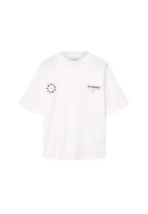 Hvit T-skjorte med kort erme laget av bomull. Den har svarte trykte logoer på forsiden og venstre erme, med en avslappet og boxy passform.