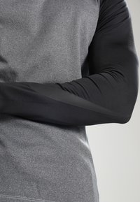 Camiseta deportiva de manga larga con un cuerpo de color gris jaspeado y mangas ajustadas negras, con una textura suave y detalles de diseño sutiles.