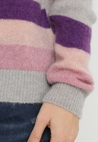 Sweter w paski w kolorze szarym, różowym i fioletowym. Wykonany z miękkiego materiału o prążkowanej fakturze. Posiada szerokie mankiety i okrągły dekolt.