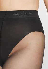 Czarne majtki z wysokim stanem z przezroczystymi panelami, z teksturowanym paskiem w talii z szarym logo "Calvin Klein".