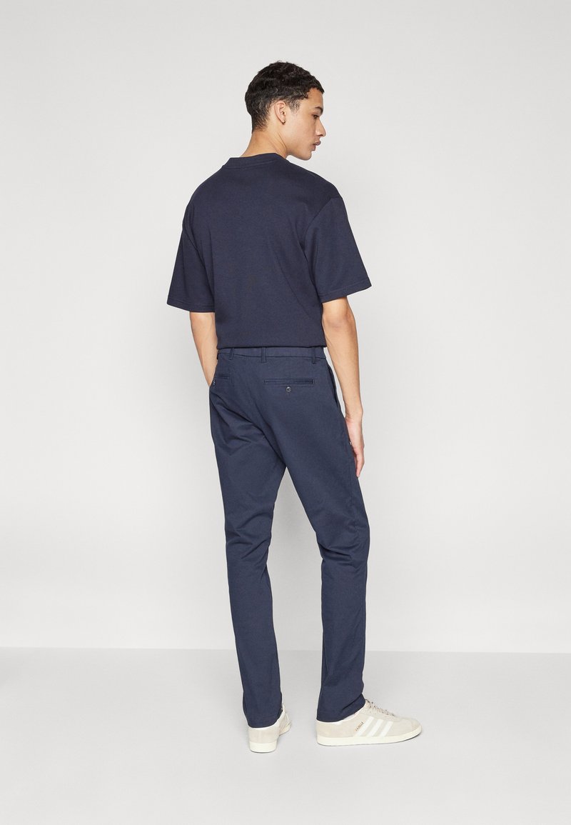 T-shirt en coton marine à manches courtes, associé à un pantalon slim fit marine et des sneakers de couleur claire, vu de dos.