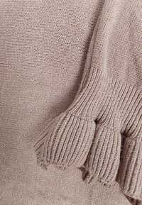 Jasnobrązowa dzianinowa tkanina sweterkowa o gładkiej, prążkowanej fakturze i bufiastych rękawach, z wzorem przypominającym muszelkę na mankietach.