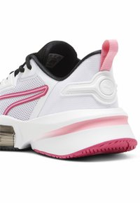 Zapatilla blanca con material de malla, acentos en negro y detalles en rosa. Presenta una suela curvada y un contrafuerte acolchado para mayor soporte.