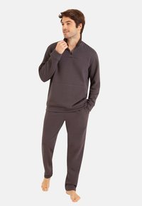 Sweatshirt gris foncé avec une fermeture éclair au col, associé à un pantalon assorti. Texture douce, coupe décontractée, avec une poche avant.