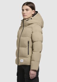 Beige Puffer-Jacke mit Kapuze, ausgestattet mit einem Frontreißverschluss und seitlichen Taschen. Weicher, gesteppten Textur mit einem Logopatch unten links.