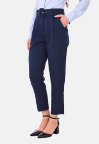 Pantaloni a vita alta blu navy con una cintura larga, pieghe frontali e tasche laterali. Indossati con scarpe con tacco a blocco nere.