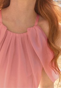 Blouse rose sans manches en tissu doux et transparent, design plissé au niveau du col, avec des drapés fluides sur les épaules, créant une coupe ample.