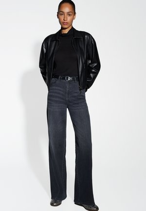 Black leather zip-up jacket, fitted black top, high-waisted dark denim jeans with wide legs, and black footwear. Simple, modern design.