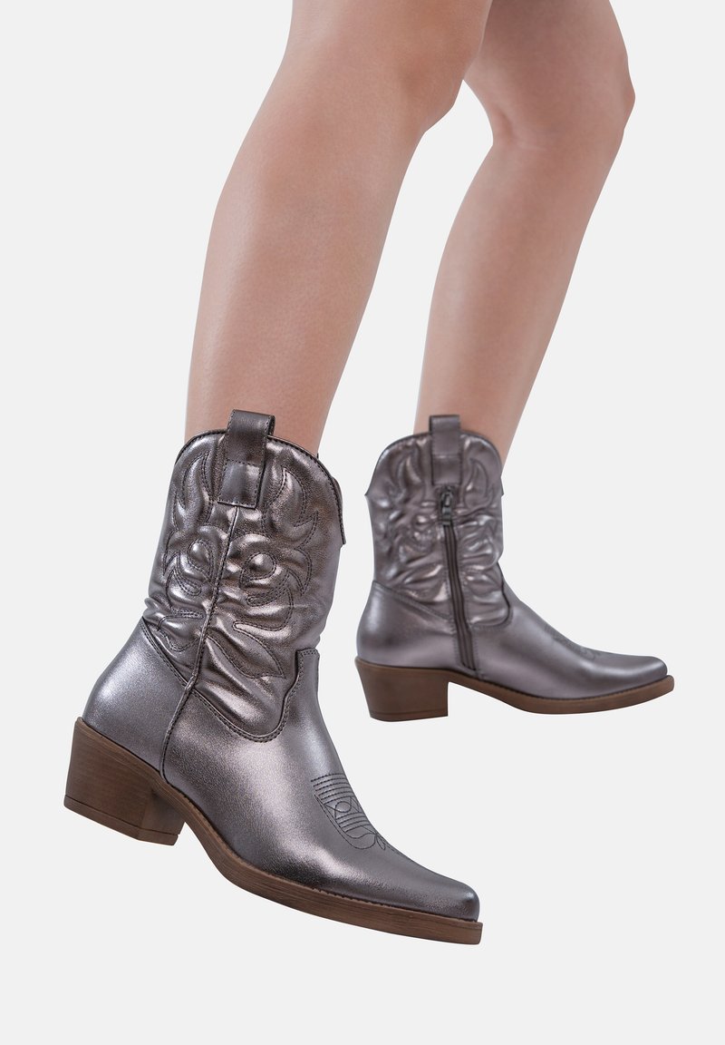 Botas de vaquera plateadas metálicas con punta afilada, detalle texturizado en el caña y tacón bajo cuadrado, con cremallera lateral para el cierre.
