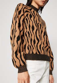 Stickad tröja i beige med svarta vågiga ränder, med ribbad rund halsringning och muddar, samt en avslappnad passform.