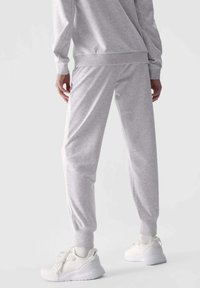 Hellgraue Jogginghosen aus weichem Stoff mit Bündchen am Knöchel, kombiniert mit weißen Sportschuhen mit strukturiertem Design.