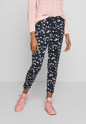 Marinblå byxor med blommönster i vitt och pastellfärger, med elastisk midja och ankellång design, kombinerat med rosa sneakers.