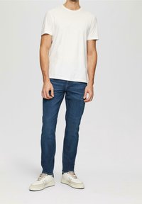 White cotton t-shirt, blue denim jeans, and beige sneakers. The t-shirt has a round neck and short sleeves, while the jeans are slim-fit.