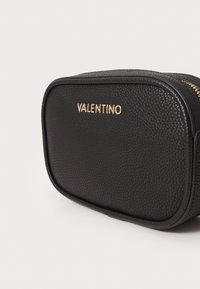 Must usu tekstuuriga must nahast kott, mille kuju on ristkülikuline. Esiküljel kuldne "VALENTINO" logo ja peal zipp.
