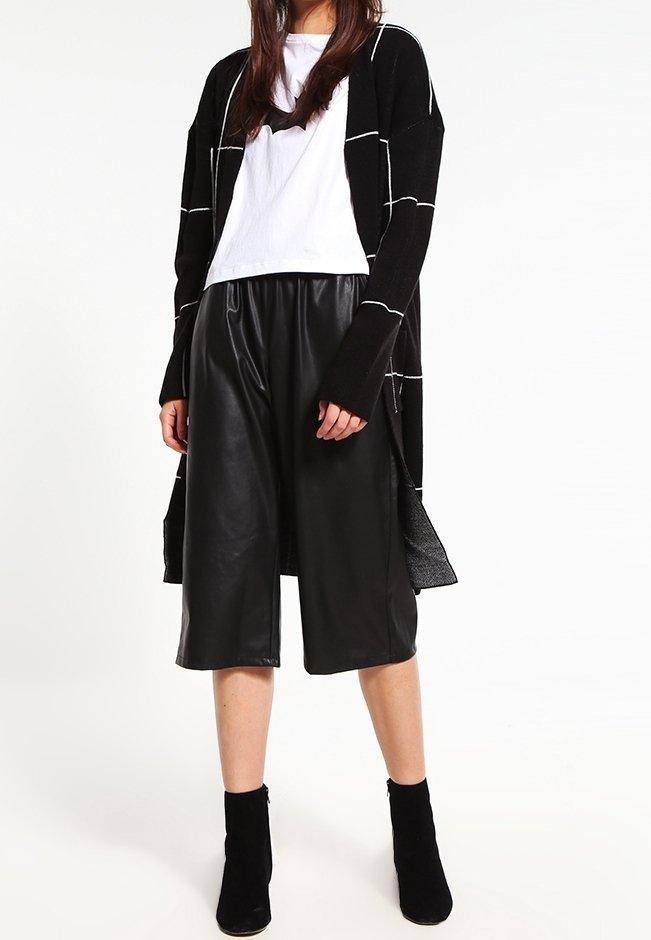 Svart lång kappa med vit rutmönster, vit t-shirt, svarta fusk-läder culotter och svarta ankelboots. Släta texturer och lagerdesign.