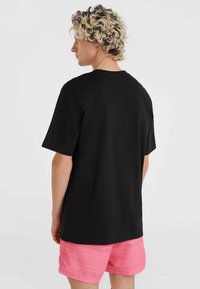 Camiseta de algodón negra con mangas cortas y cuello redondo, combinada con pantalones cortos rosas con rayas horizontales blancas y texto.