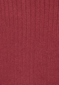 Ribbformat textil i en dämpad röd nyans. Texturen är mjuk med vertikala ränder som visar ett stickat mönster.