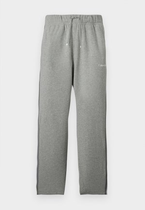 Jasnoszare spodnie dresowe z elastycznym pasem, sznurkiem do ściągania, czarnymi paskami po bokach i małym białym logo Calvin Klein z przodu.
