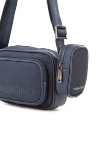Borsa a tracolla blu navy con tessuto testurizzato, due scomparti con zip e dettagli brandizzati. Cinghia regolabile per un trasporto comodo.