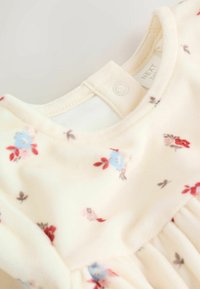 Puha krém színű baba ruha kék, piros és rózsaszín virágmintákkal, nyakrészén patent gombbal a könnyű nyitás érdekében.