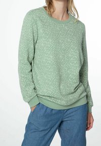 Sweat-shirt vert avec un motif tacheté blanc, col rond et poignets côtelés. Associé à un pantalon bleu clair. Tissu doux, coupe décontractée.