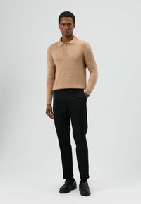 Beige gebreide trui met een kraag en knoopdetail, gecombineerd met op maat gemaakte zwarte broek en zwarte schoenen. Gladde textuur, minimalistisch ontwerp.