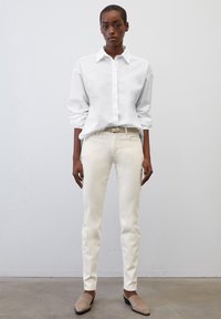 Camisa blanca de manga larga con botones, pantalones ajustados crema y zapatos sin tacón beige. Diseño simple con una textura suave y un ajuste entallado.