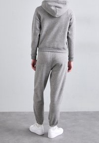 Grå sweatshirt och sweatpants-set tillverkat av mjukt material, med huva, ribbade ärmslut och öppningar vid anklarna, kombinerat med vita sneakers.