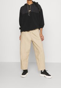 Černá mikina s kapucí s texturovaným horním panelem, béžové kalhoty s volným střihem a černé tenisky s b ílými podrážkami.