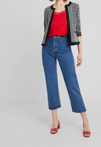 Czarna i biała marynarka z tweedu, do niej jednolity czerwony koronkowy top na ramiączkach, zestawione z wysokim stanem niebieskich jeansów o prostych nogawkach oraz czerwonymi butami na cienkich paskach.